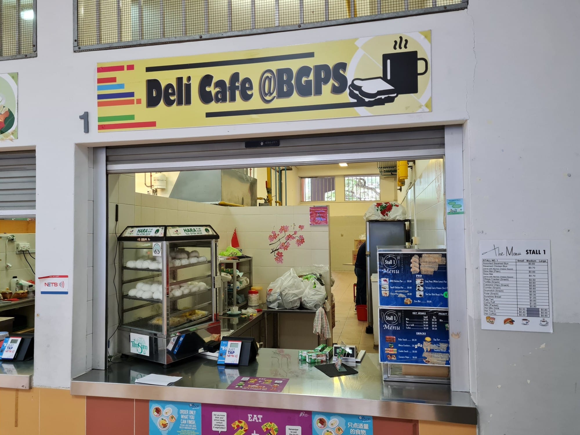 A canteen stall called Deli Cafe @BGPS with steamed bun warmers, a menu board, and a service counter.